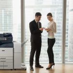 Zwei Personen in Geschäftskleidung diskutieren Dokumente in einem Büro neben einem Multifunktionsdrucker der Serie Xerox® AltaLink® B8200 Zwei Personen in Geschäftskleidung diskutieren Dokumente in einem Büro neben einem Multifunktionsdrucker der Serie Xerox® AltaLink® B8200
