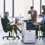 Xerox® VersaLink® C7100 Serie, Farb-Multifunktionsdrucker für den Arbeitsplatz Teamarbeit in einem Büro mit bedruckten Papieren und dem Farb-Multifunktionsdrucker Xerox® VersaLink® C7100 Series